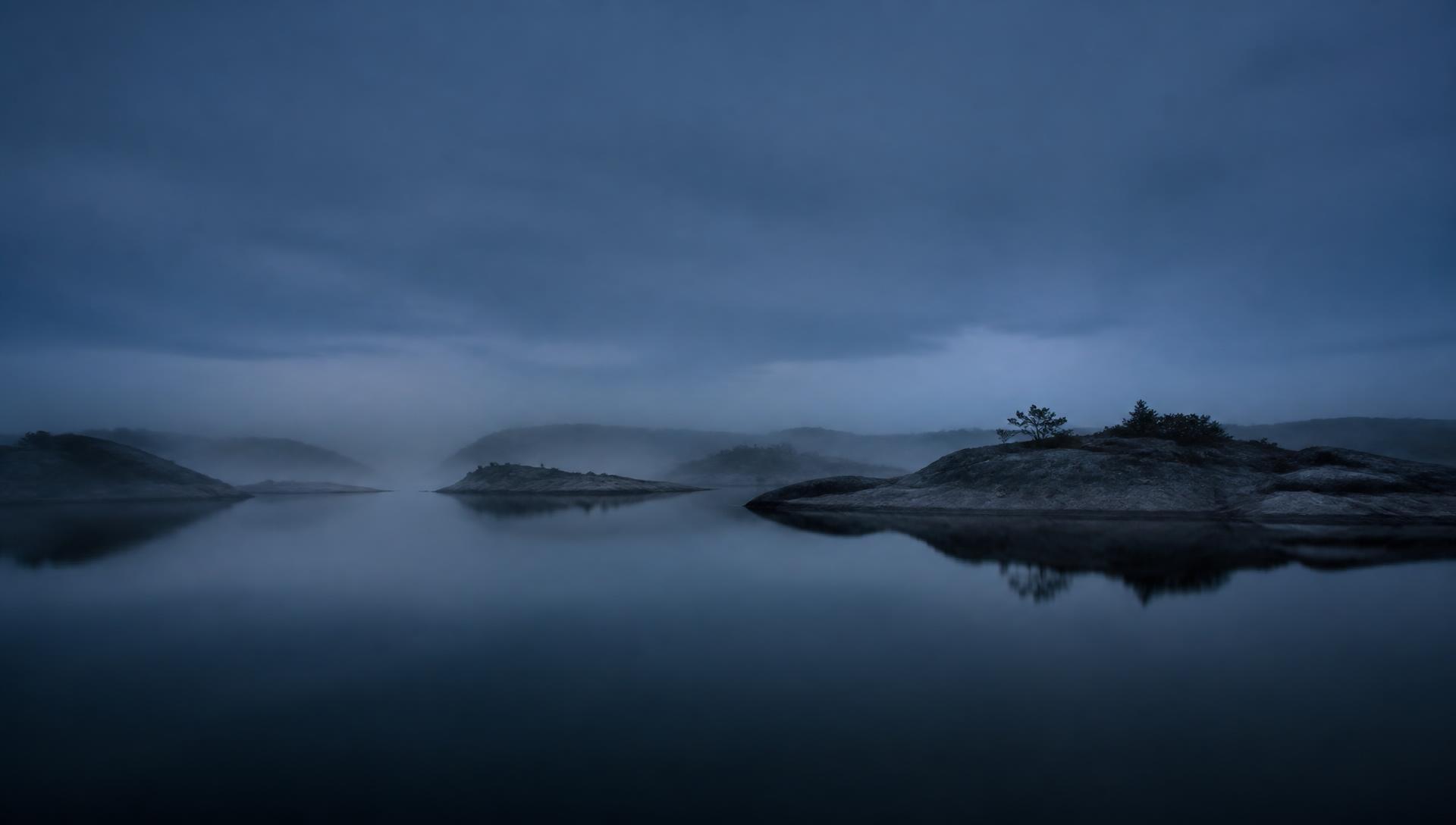 Still water and low fog over granite islands at blue hour